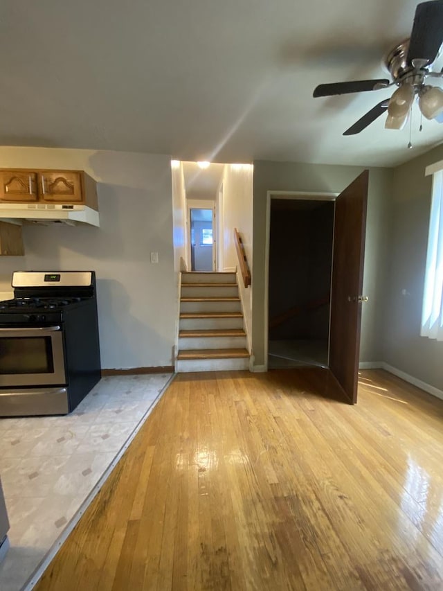 unfurnished living room featuring light wood-type flooring, baseboards, a ceiling fan, and stairway