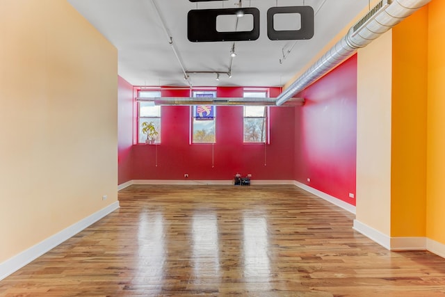 unfurnished room featuring rail lighting, baseboards, and wood finished floors