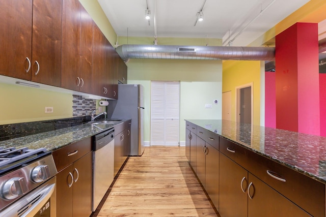 kitchen with a sink, stainless steel appliances, dark stone counters, visible vents, and light wood finished floors
