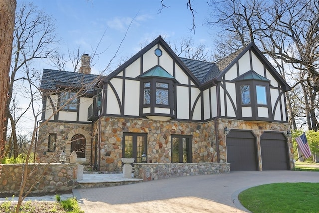 view of front facade with stucco siding, stone siding, french doors, a chimney, and curved driveway