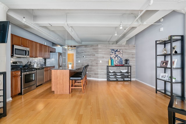 kitchen with appliances with stainless steel finishes, brown cabinetry, track lighting, and light wood-style floors