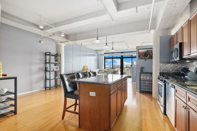 kitchen with appliances with stainless steel finishes, a kitchen breakfast bar, light wood finished floors, decorative backsplash, and brown cabinetry