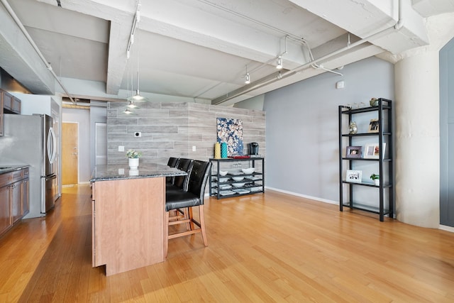 kitchen with freestanding refrigerator, a breakfast bar area, light wood-type flooring, dark stone countertops, and a center island