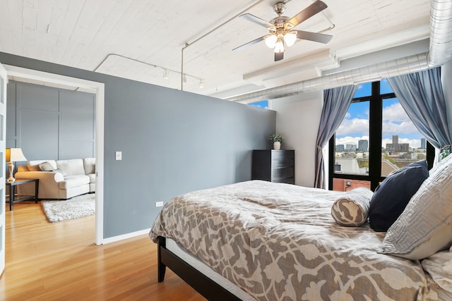 bedroom with wood finished floors, baseboards, a city view, track lighting, and a ceiling fan