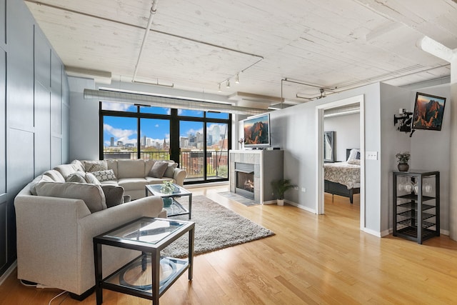 living area featuring track lighting, light wood-style flooring, a tile fireplace, and baseboards