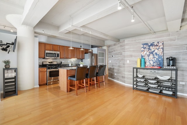 kitchen featuring rail lighting, stainless steel appliances, a kitchen bar, brown cabinets, and light wood-type flooring