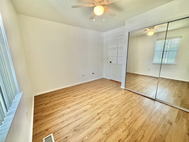 unfurnished bedroom with a closet, wood finished floors, visible vents, a ceiling fan, and baseboards