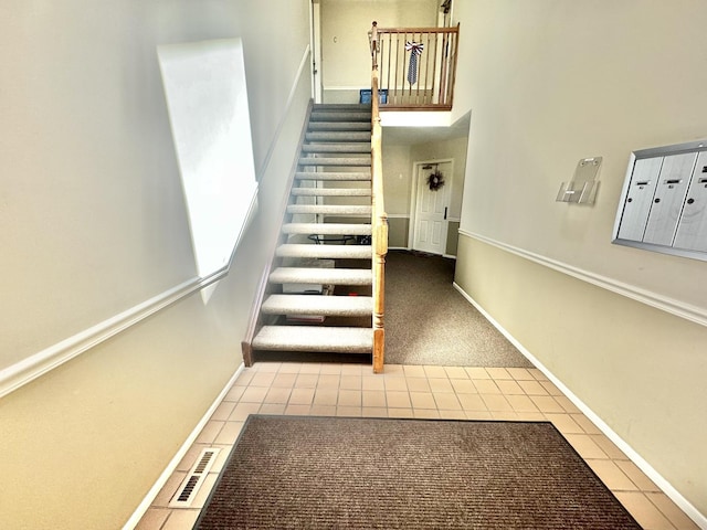 staircase with a towering ceiling, visible vents, mail area, tile patterned floors, and baseboards