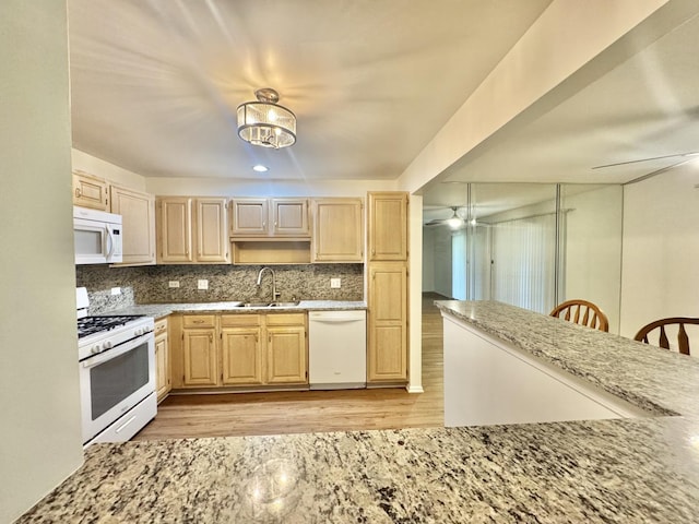 kitchen with a sink, white appliances, light brown cabinetry, and light wood-style floors