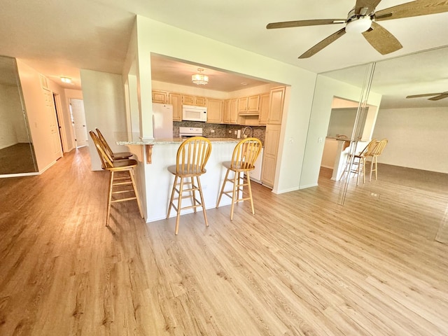 kitchen featuring a breakfast bar area, light wood-style flooring, light brown cabinets, ceiling fan, and white appliances