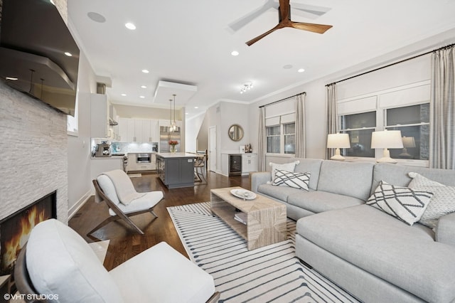 living room featuring dark wood-style floors, ceiling fan, wine cooler, a stone fireplace, and ornamental molding