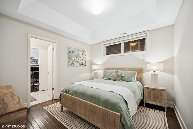 bedroom with a raised ceiling, dark wood-style flooring, and baseboards