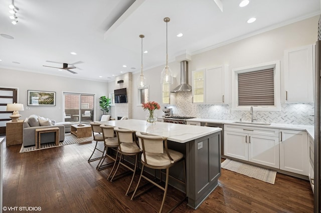 kitchen with wall chimney exhaust hood, a sink, open floor plan, a breakfast bar, and backsplash