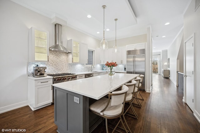 kitchen featuring wall chimney exhaust hood, appliances with stainless steel finishes, a kitchen island, a sink, and a kitchen bar