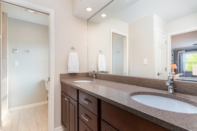 bathroom featuring a sink, double vanity, toilet, and baseboards