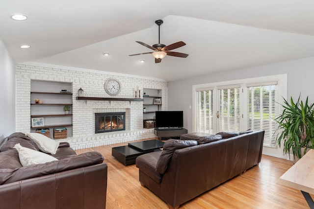 living room with a ceiling fan, light wood-style flooring, lofted ceiling, and a brick fireplace