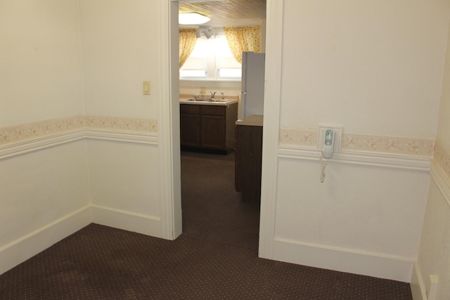 corridor featuring a decorative wall, dark colored carpet, wainscoting, and a sink