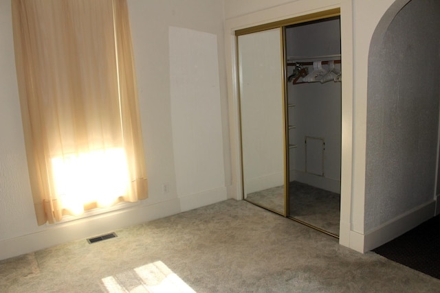 unfurnished bedroom with carpet, visible vents, arched walkways, and a closet