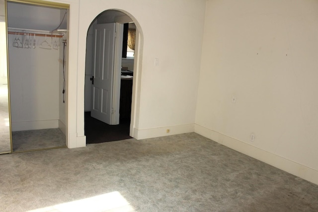 unfurnished bedroom featuring arched walkways, carpet flooring, and a closet