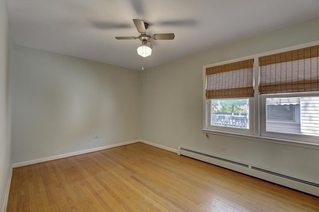 unfurnished room with a baseboard heating unit, healthy amount of natural light, wood finished floors, and baseboards