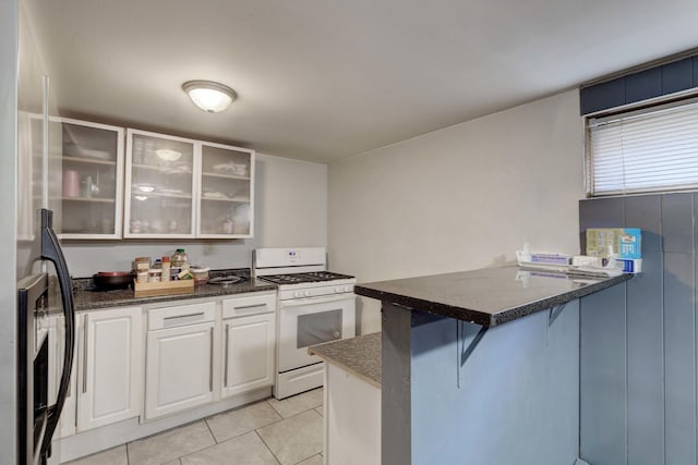 kitchen featuring white gas range oven, a peninsula, light tile patterned floors, a kitchen breakfast bar, and white cabinets