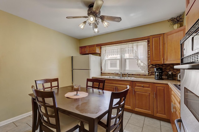kitchen with a sink, freestanding refrigerator, light tile patterned floors, ceiling fan, and decorative backsplash