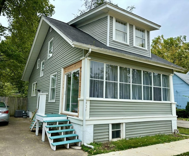 view of property exterior with central AC unit, roof with shingles, fence, and a sunroom