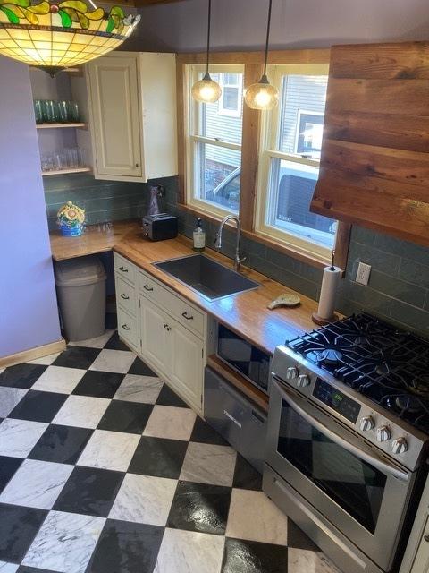 kitchen with white cabinets, backsplash, stainless steel gas range oven, and a sink