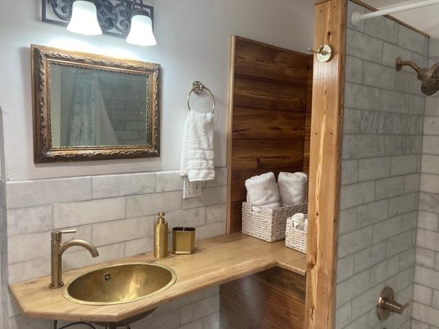 full bathroom featuring tiled shower, decorative backsplash, and a sink