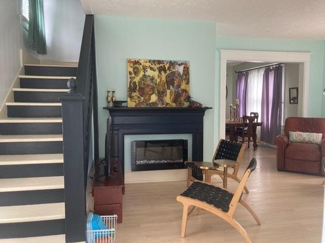 living area with stairs, a textured ceiling, a glass covered fireplace, and wood finished floors