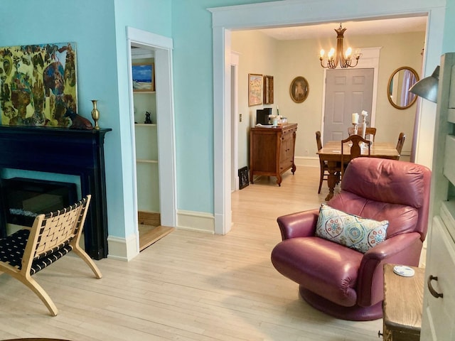 living area with a fireplace, a notable chandelier, baseboards, and wood finished floors
