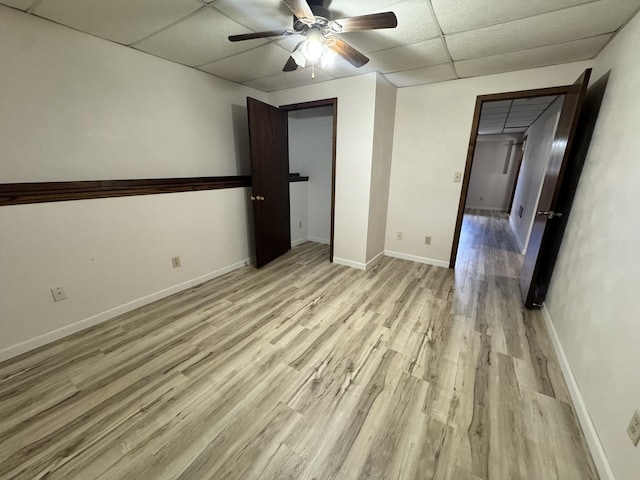 unfurnished bedroom featuring light wood finished floors, baseboards, a ceiling fan, and a drop ceiling