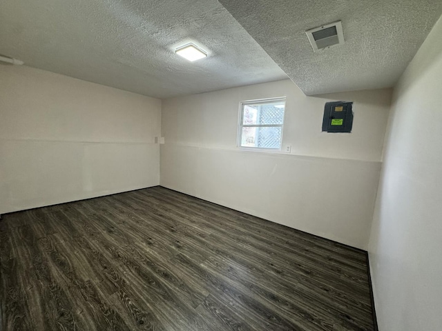 basement with electric panel, a textured ceiling, dark wood-type flooring, and visible vents