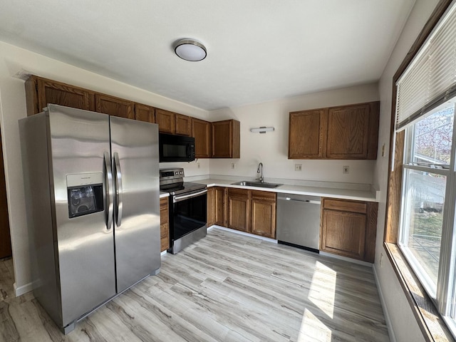 kitchen featuring light wood finished floors, plenty of natural light, stainless steel appliances, and a sink