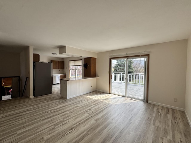unfurnished living room featuring a wealth of natural light, baseboards, and light wood-style floors