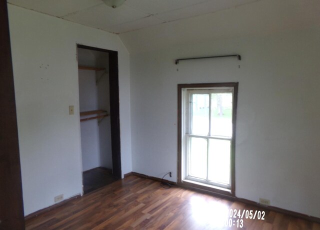 unfurnished bedroom with dark wood-style flooring, a closet, baseboards, and vaulted ceiling