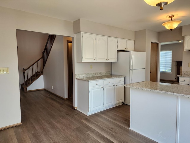 kitchen featuring dark wood finished floors, white cabinetry, freestanding refrigerator, baseboards, and light stone counters