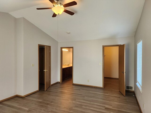 unfurnished bedroom with vaulted ceiling, wood finished floors, baseboards, ensuite bathroom, and a ceiling fan