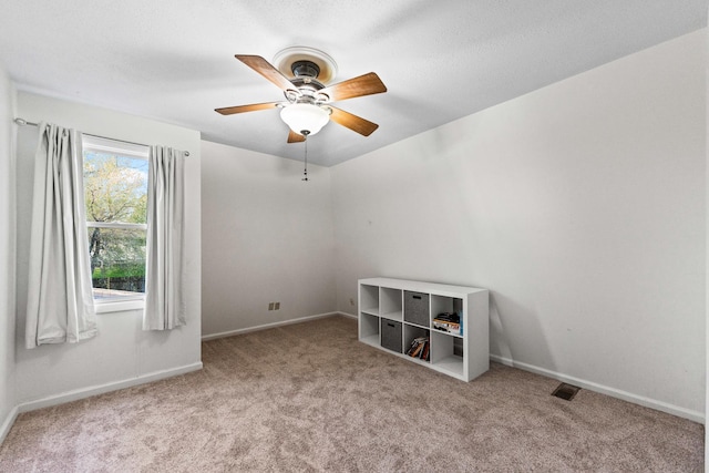 carpeted spare room with visible vents, baseboards, and a ceiling fan