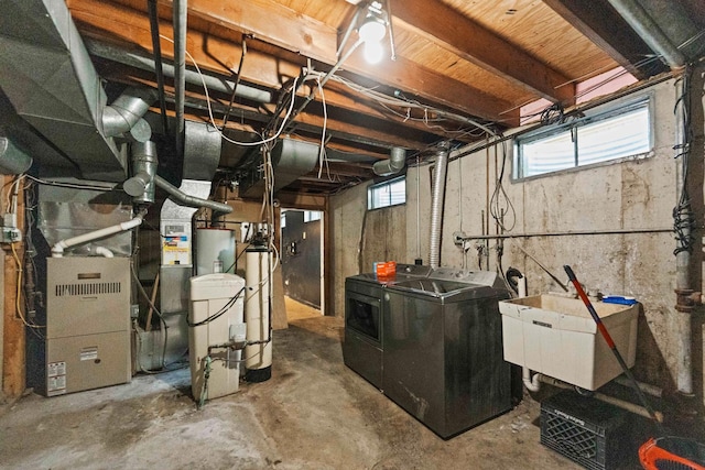 basement featuring heating unit, washing machine and clothes dryer, water heater, and a sink