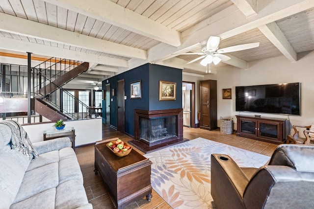 living room featuring stairs, wood finished floors, ceiling fan, beamed ceiling, and a multi sided fireplace