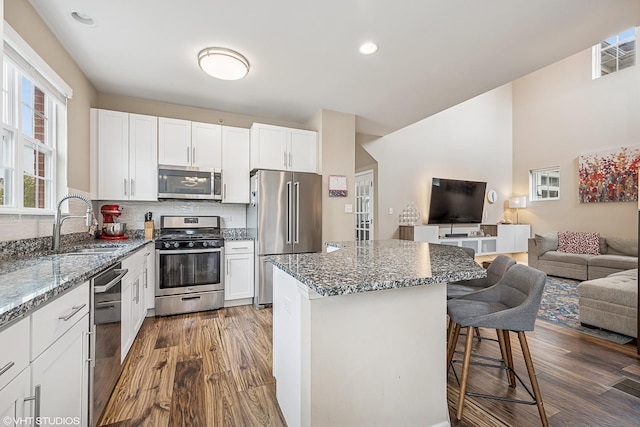 kitchen featuring appliances with stainless steel finishes, a sink, open floor plan, a breakfast bar, and dark wood-type flooring