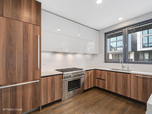 kitchen with a sink, modern cabinets, high end range, backsplash, and light countertops