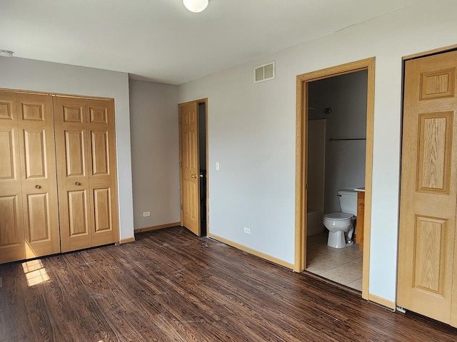 unfurnished bedroom with dark wood finished floors, baseboards, a closet, and ensuite bath