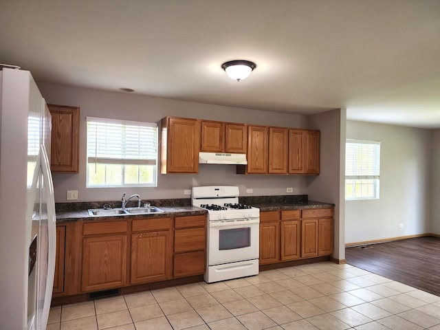 kitchen with fridge with ice dispenser, white gas range, a sink, under cabinet range hood, and brown cabinets
