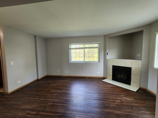 unfurnished living room featuring wood finished floors, a tiled fireplace, and baseboards
