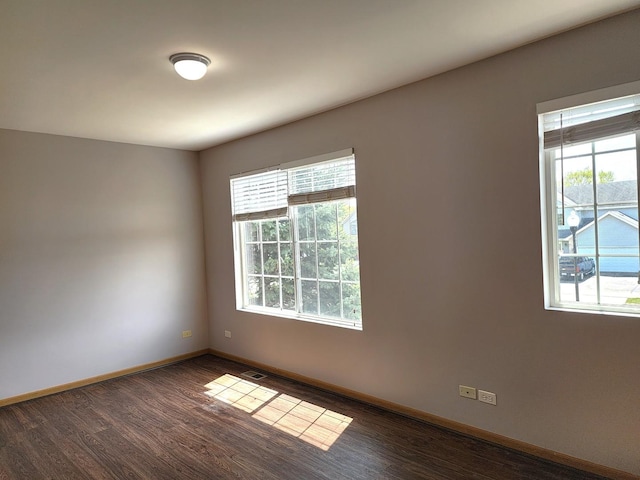 empty room featuring healthy amount of natural light, dark wood finished floors, and baseboards