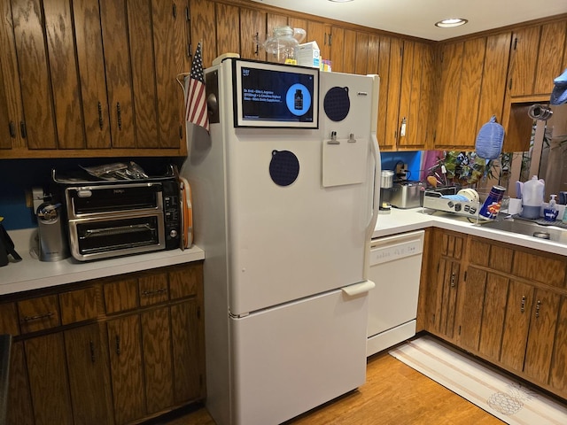 kitchen with a sink, brown cabinetry, light wood-type flooring, white appliances, and light countertops