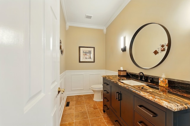 bathroom with crown molding, vanity, toilet, wainscoting, and a decorative wall