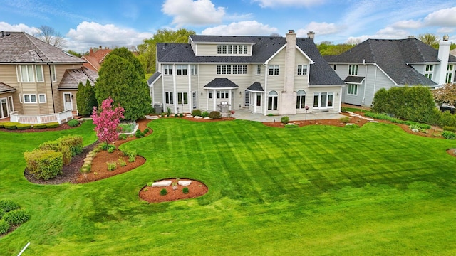 back of house featuring a patio, a chimney, a lawn, and a shingled roof
